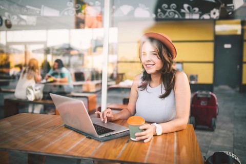 Beautiful young caucasian woman sitting on a terrace in a cafe in summer at a wooden table in a hat