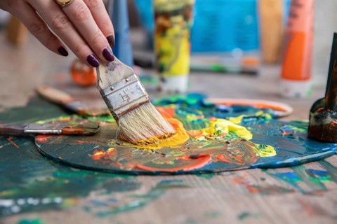 A detailed closeup of a hand skillfully mixing together vibrant and colorful paints on a palette
