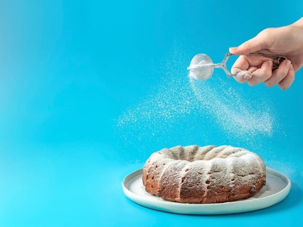 Woman's hand sprinkling icing sugar over fresh home made bundt cake. Powder sugar falls on fresh