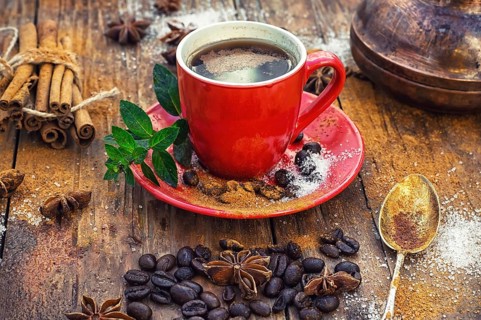 Red glass Cup with coffee on wooden background strewn with aromatic spices to drink