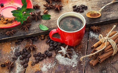 Red glass Cup with coffee on wooden background strewn with aromatic spices to drink