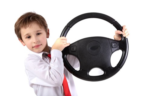 Funny little boy holding a car steering wheel. Young driver on a white background