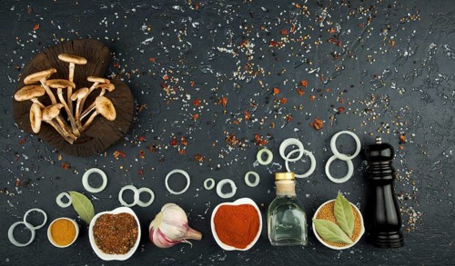Fresh mushrooms with spices and herbs on black board. View from above. Copy space