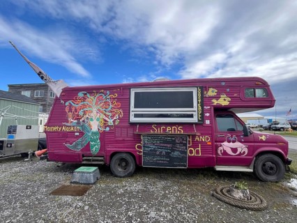 Food truck with colourful wall art and a menu in front of a cloudy street, Homer, Alaska, USA,
