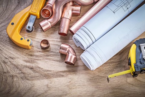 Construction drawings measuring tape copper water pipe cutter fittings on wooden board plumbing