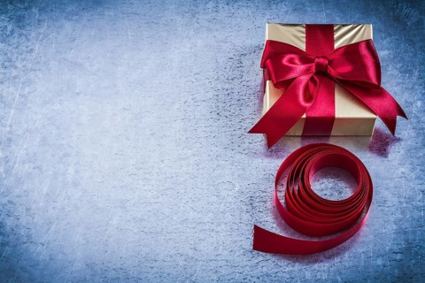 Present box with rolled red tape on metallic background copyspace
