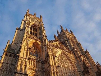 A front view of the towers at the entrance to york minster in sunlight against a blue cloudy sky