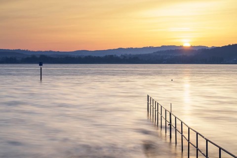 Sunrise over a calm lake with railings and distant hills, lido, Litzelstetten, Lake Constance,