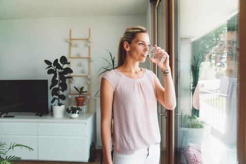 Smiling young caucasian woman taking her morning supplements, vitamin pills with a glass of water