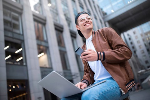 Happy handsome student looking at computer screen while typing something on laptop keyboard during