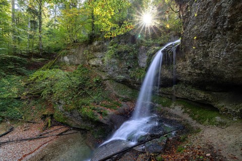 A waterfall in the forest with sunbeams through the trees, peaceful and natural, Hasenreuter