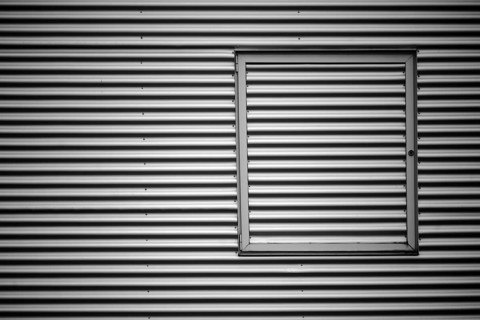 Close-up of the corrugated sheet metal façade of an industrial building with a metal window frame