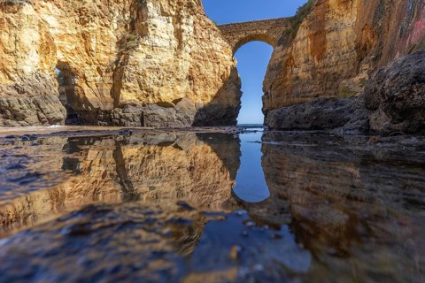 Yellow rocks and cliffs on a sandy beach. A bay by the sea, over which the old stone bridge of the
