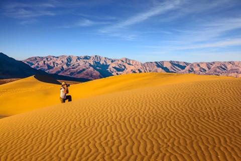 Woman in striped shirt and straw hat photographing sand waves. Bright morning in picturesque part