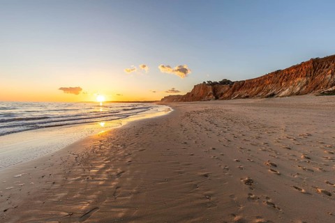 Beautiful sandy beach with red rocks and cliffs. Twilight at sunset with shallow waves on the