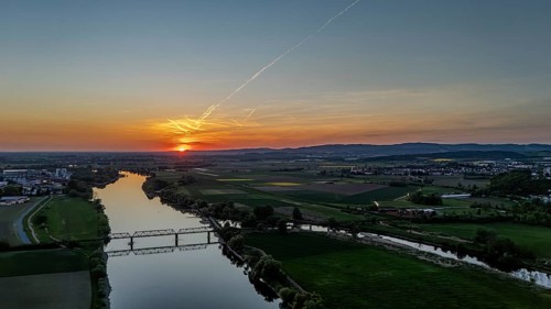 View of river and railway bridge in the light of a warm sunset, framed by fields, Danube, Bogen,