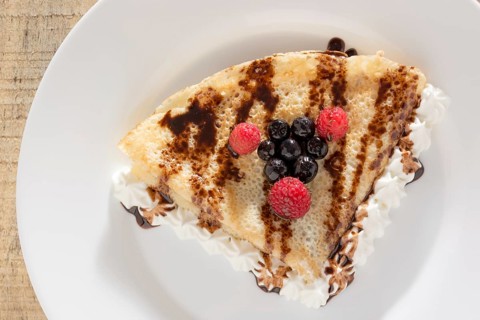 Fresh, golden pancakes with fruit and cream on a white plate with blurred background