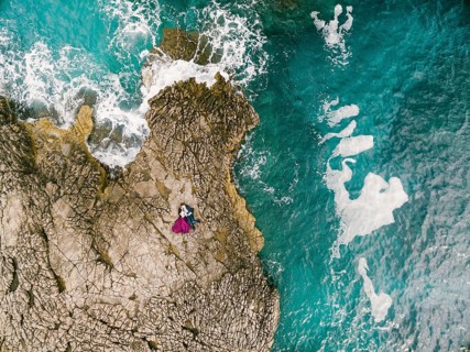 Man and woman lie embracing on the rocks by the blue foaming sea. View from above.