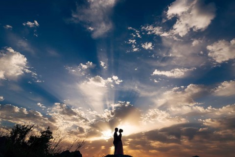 The bride and groom tenderly hug on the mountain in the rays of the setting sun.