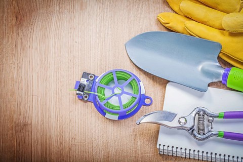 Protective gloves pruning shears garden tie wire hand shovel notepad on wooden board gardening