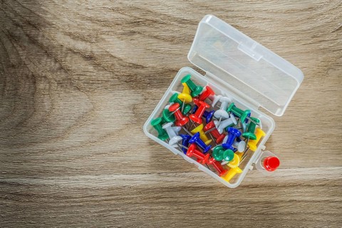 Set of drawing pins in plastic box on wooden board
