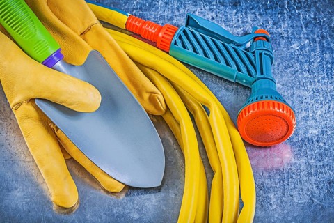 Set of rubber garden hose spray nozzle safety gloves spade on metallic background gardening concept