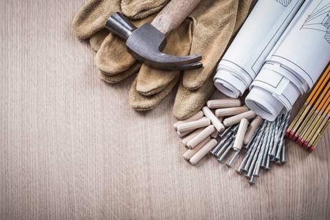 Wooden meter dowels blueprint rolls claw hammer leather protective gloves and metal nails on wood