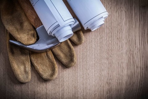 Construction drawings protective gloves and claw hammer on wooden board