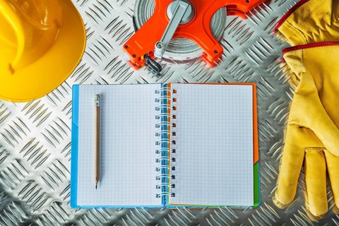 Safety gloves hard hat tape measure notebook pencil on corrugated metal sheet