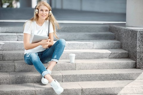 Happy young woman with vintage headphones and a cup of coffee to go, surfing the internet on a