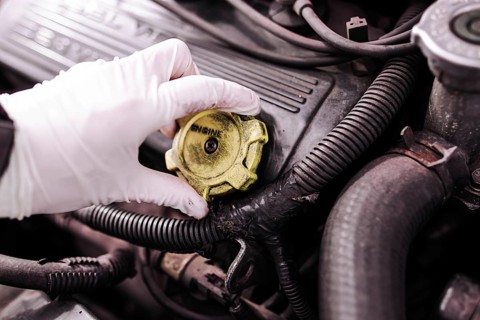 A gloved hand removing the cap from a car engine for maintenance