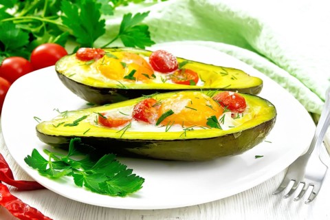 Scrambled eggs with cherry tomatoes in two halves of avocado in a plate, green towel and fork on