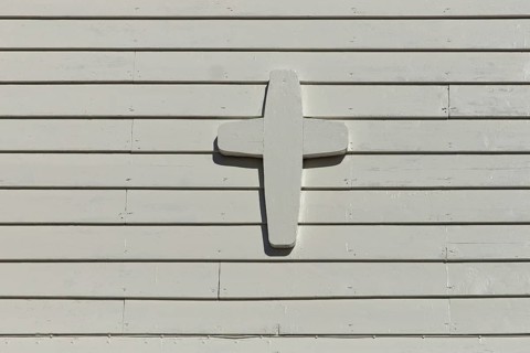 Closeup of white painted wood cross on a white wooden wall