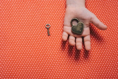 Hand holding a heart shaped lock and key on a red background