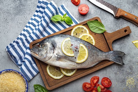 Raw fish dorado with ingredients lemon, fresh basil, cut cherry tomatoes, uncooked rice on wooden
