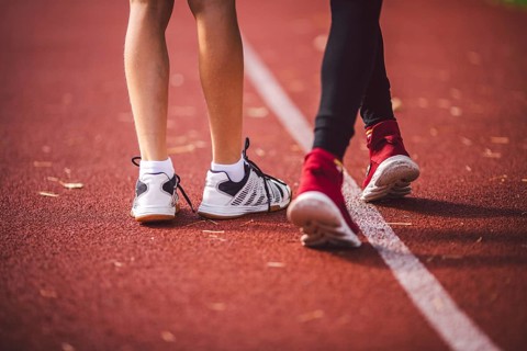 Four legs close-up brother and sister in trainers running on red treadmill in running stadium rear