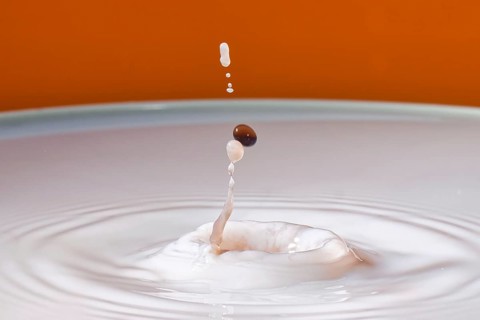 A drop with a splash in an orange environment creates dynamic fluid movement, water droplets,