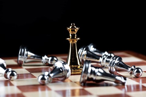Gold queen chess defeats silver figures on wooden chessboard. Intellectual duel and tactical battle