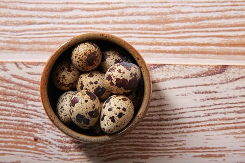 Quail eggs in a little bowl with nest shape on white wooden board