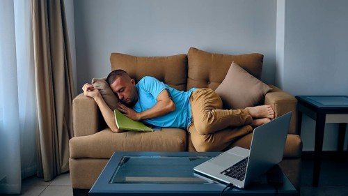 Young adult caucasian man felt asleep on a couch in front of laptoe. Tired man sleeps on sofa