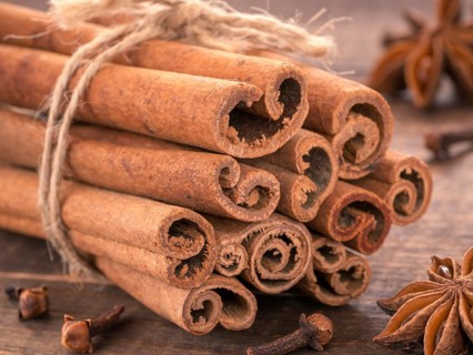 Ground cinnamon, cinnamon sticks, tied with jute rope on wooden background. Clove and star anise as