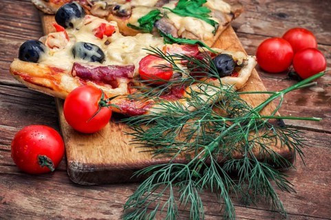 Hunk of delicious meat pizza with bacon and olives on the background of the vegetables.The image is