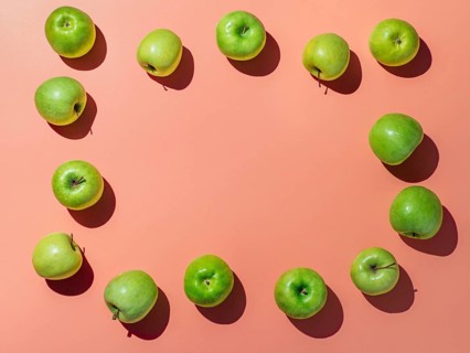 Green apples on orange or coral pink background with copy space for text or design in center,