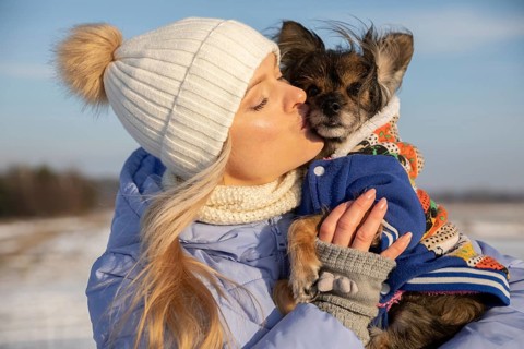 Close-up of a blonde woman hugging her dog. The woman and dog are outside on a winter day. Both are