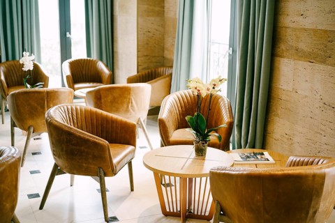 A large hall with exits to the balcony with round tables and flowers and brown armchairs made of