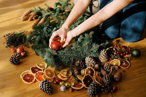 Designer is arranging the Christmas wreath while sitting on the floor. Cropped. Faceless.