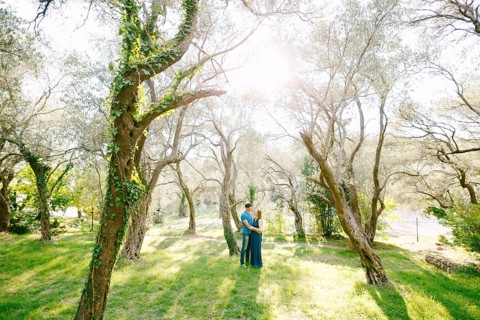 Man hugs pregnant woman in a beautiful park of green olive trees entwined with ivy on a sunny day.