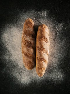 Two whole homemade buckwheat loaf bread with buckwheat flour on black textured background. Top view
