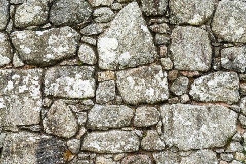A background of an old stone wall built with uneven and random blocks and stones