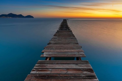 Peaceful sunrise seascape with an old wooden dock leading out into the calm ocean waters of Alcudia